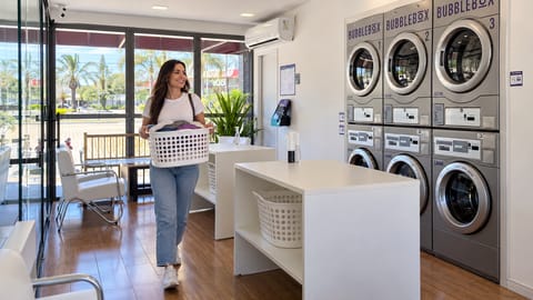 Cliente carregando cesto de roupas na lavanderia self-service Bubble Box Jacareí, com máquinas numeradas