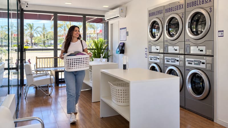 Cliente carregando cesto de roupas na lavanderia self-service Bubble Box Jacareí, com máquinas numeradas